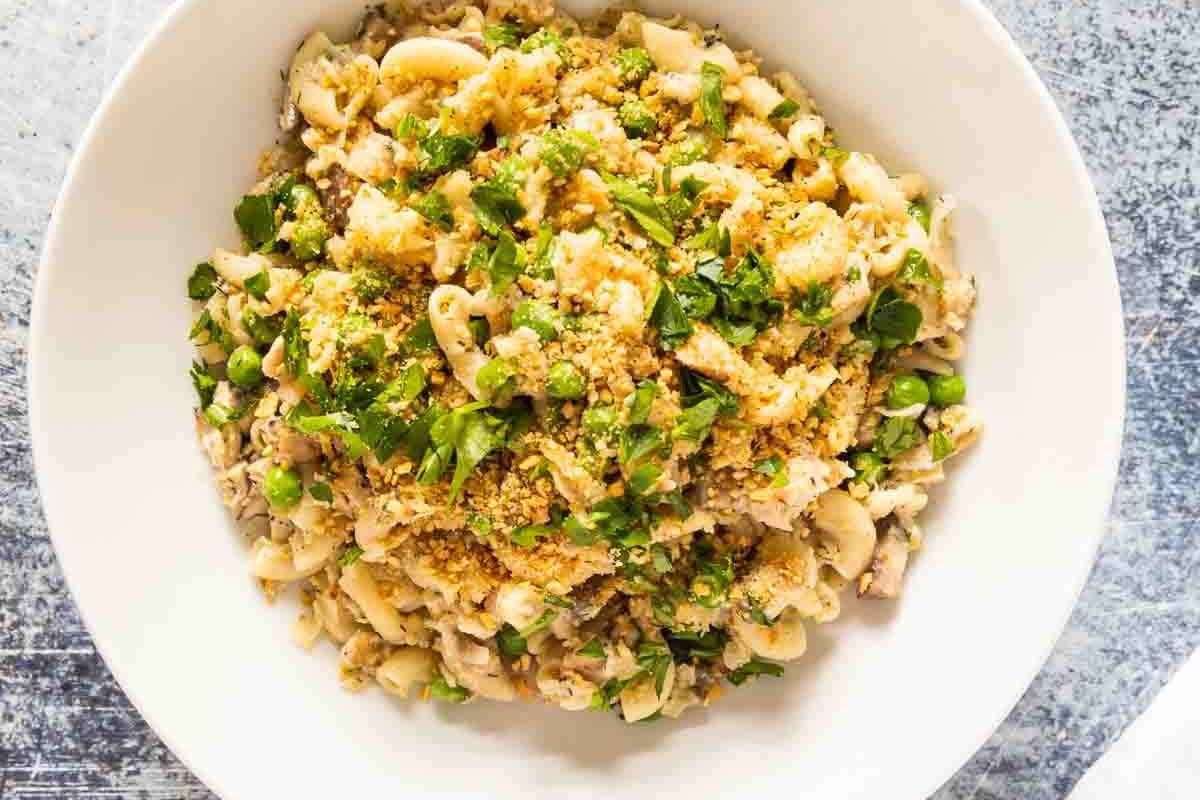 A white bowl filled with macaroni mixed with peas, breadcrumbs, and chopped herbs on a gray surface—perfect for easy dinner ideas or those searching for kid-friendly recipes the whole family will love.