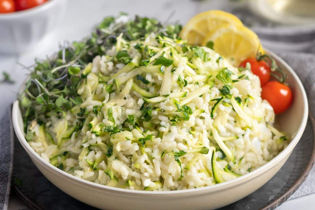 A bowl of rice mixed with shredded zucchini and herbs makes for one of the most flavorful rice dishes, garnished with microgreens, lemon slices, and cherry tomatoes. Perfect for those seeking simple rice recipes that are both fresh and delicious.
