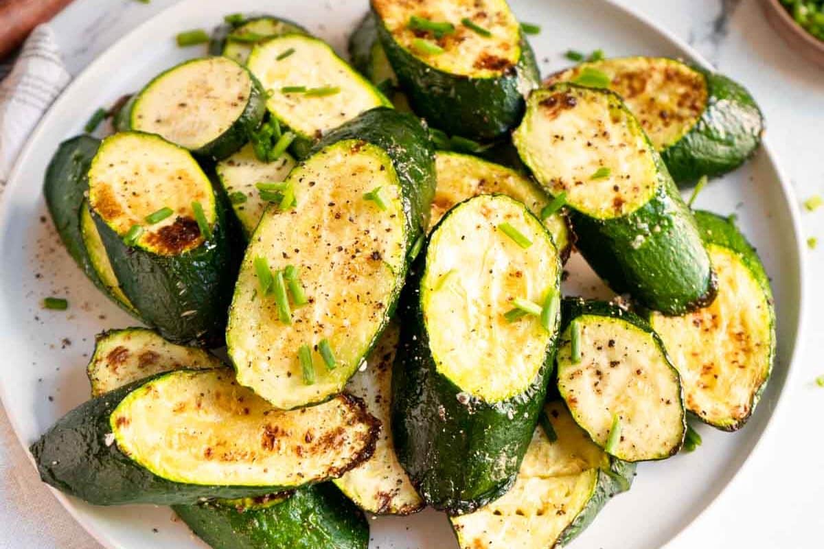 Plate of roasted zucchini slices garnished with chopped chives and black pepper—perfect for those seeking delicious roasted vegetable recipes.