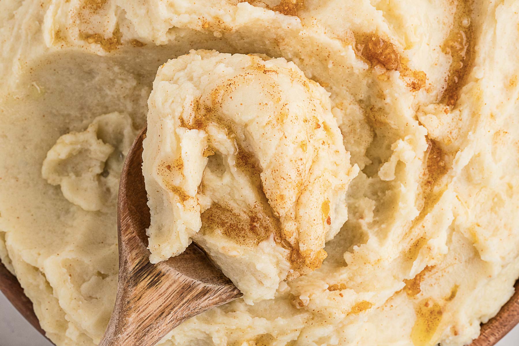 A wooden spoon lifts a scoop of buttery, cinnamon-dusted mashed potatoes, a comforting classic among potato side dishes.