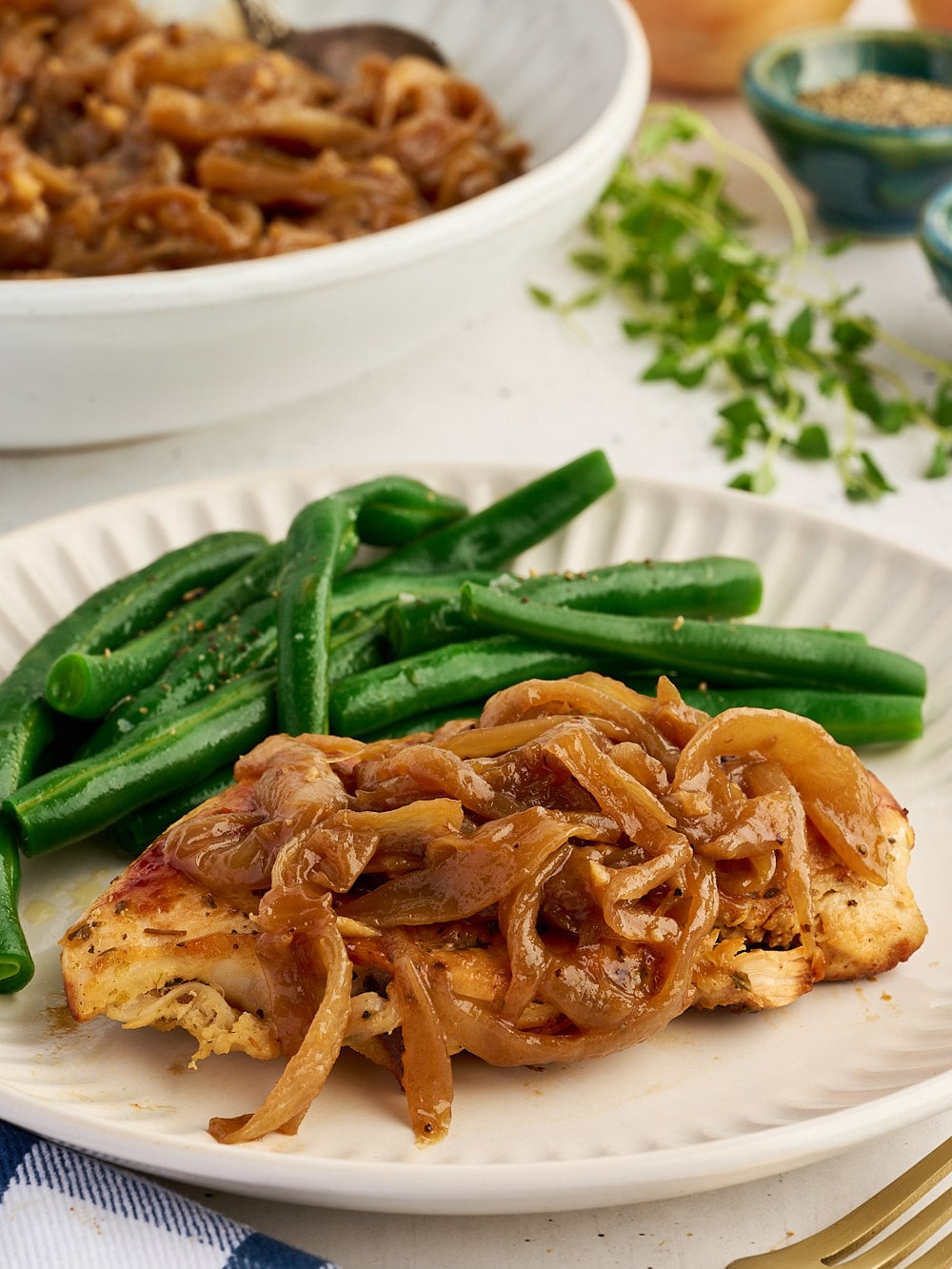 A chicken breast topped with caramelized onions, served with a side of green beans on a white plate.