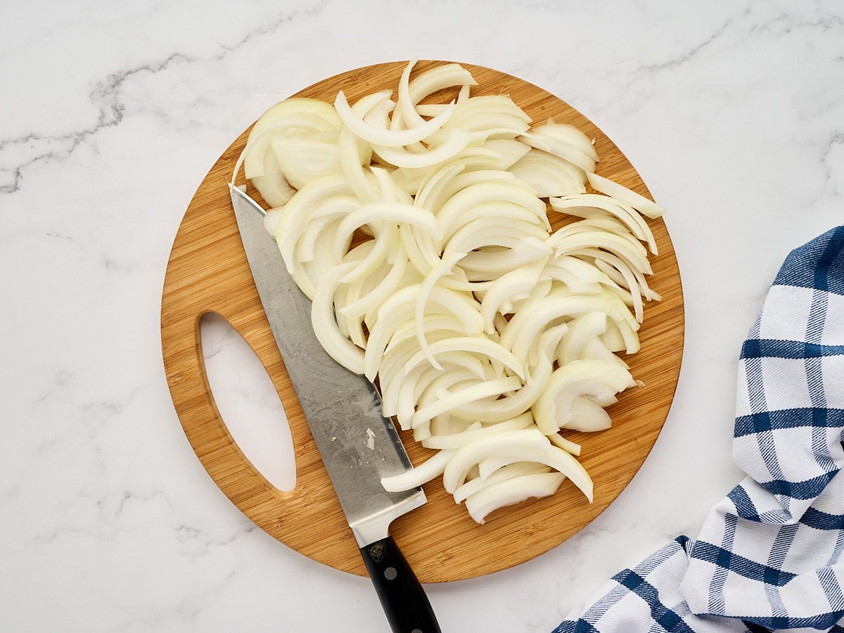 Sliced yellow onions on a wooden cutting board with a chef's knife.