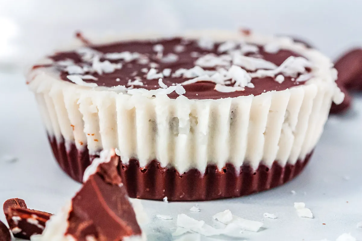 A close-up of a chocolate and coconut layered dessert cup with a fluted paper wrapper, topped with shredded coconut.