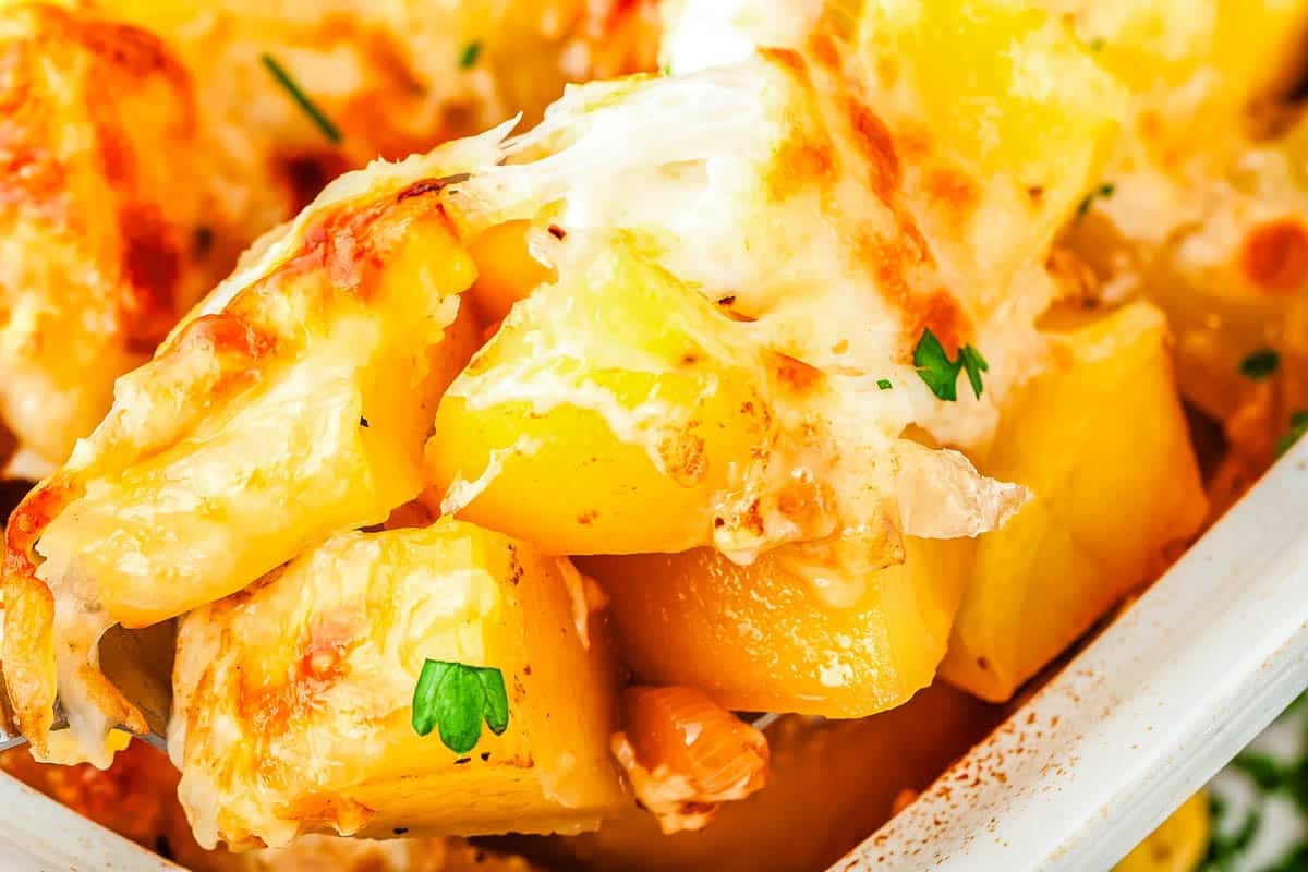 Close-up of cubed potatoes, a delicious potato side dish baked with melted cheese and topped with parsley.