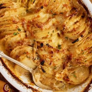 A baking dish of scalloped potatoes with a serving spoon tucked inside.