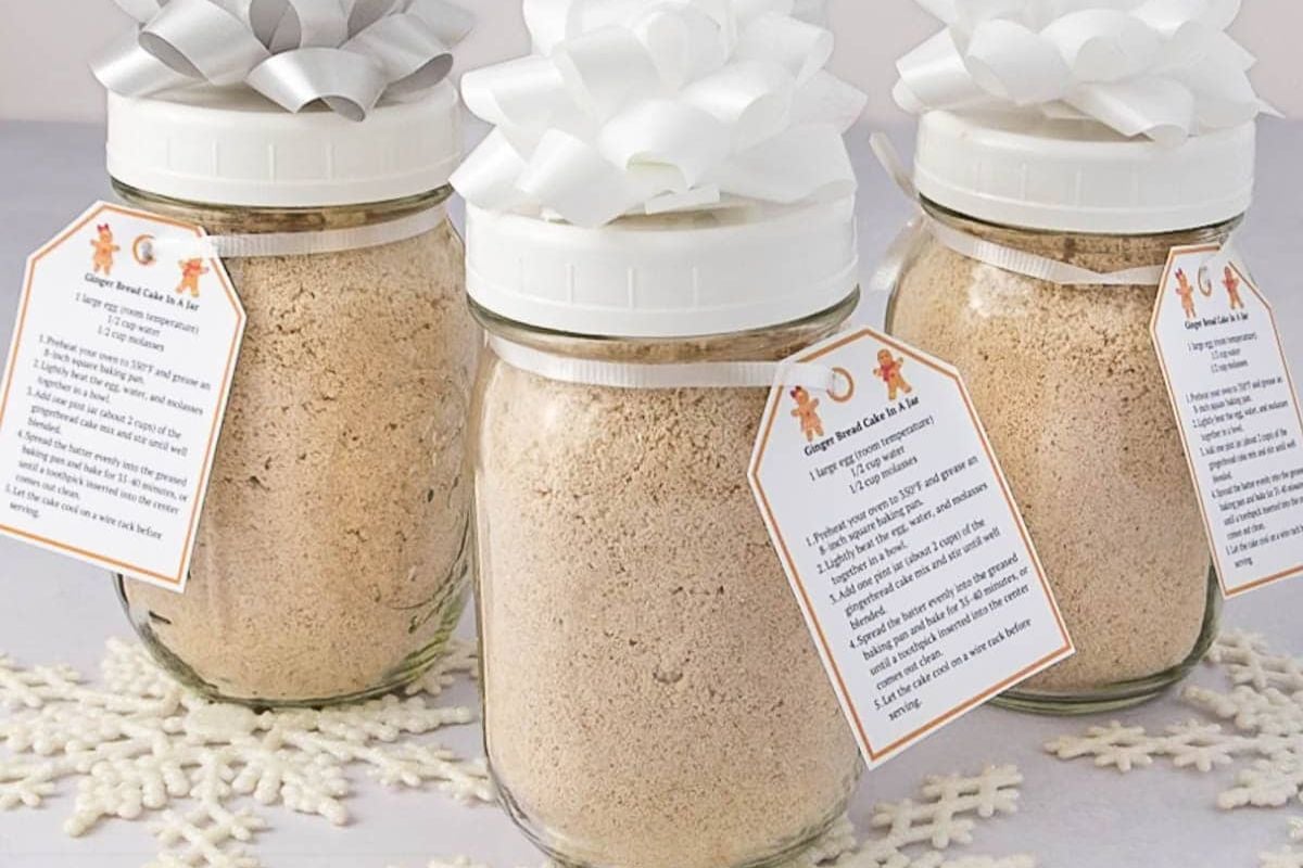 Three glass jars filled with dry gingerbread cake mix, each topped with a white ribbon and a recipe tag, make for perfect affordable hostess gifts.