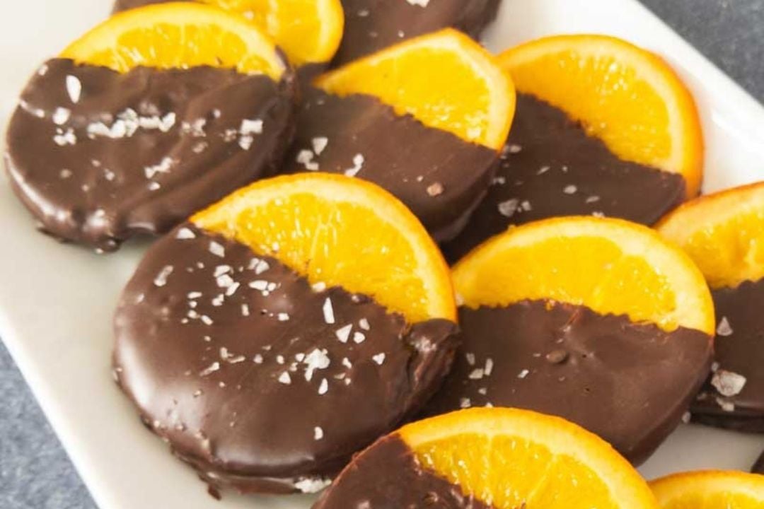 Orange slices dipped in dark chocolate and sprinkled with sea salt on a white plate.