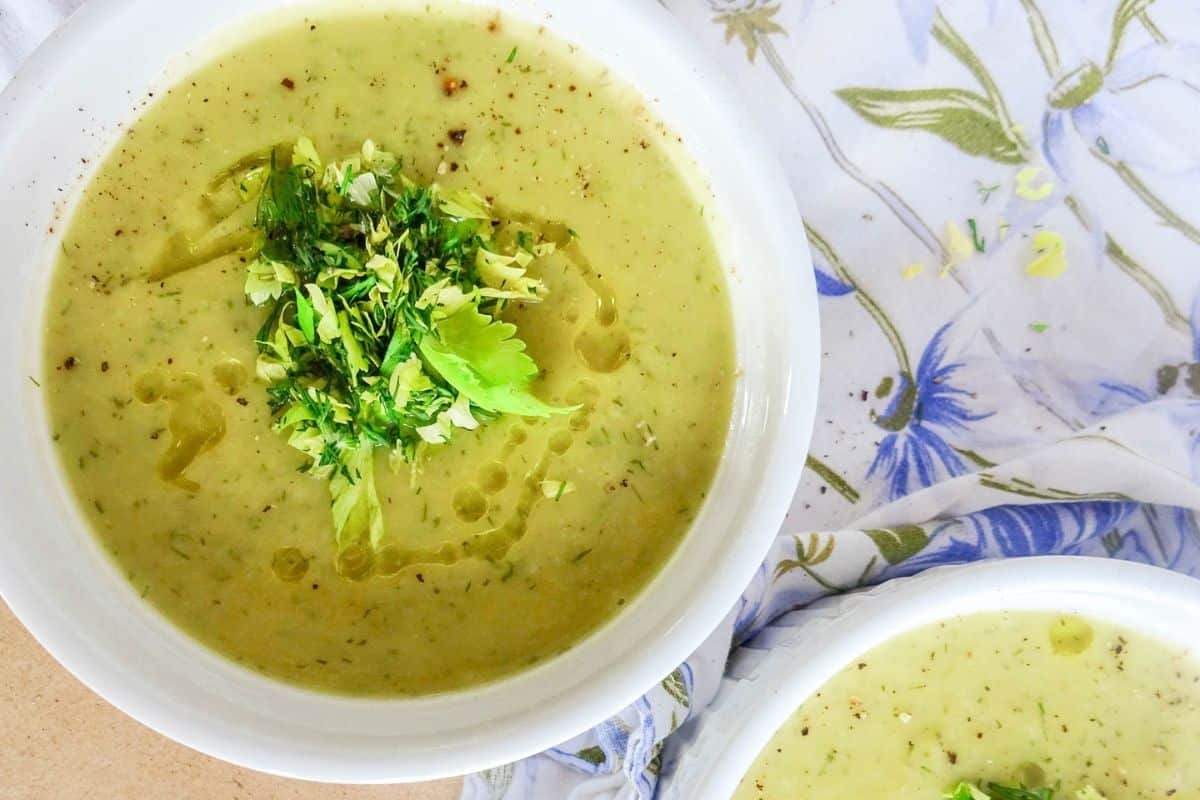 Two bowls of healthy, comforting green vegetable soup topped with fresh herbs and a drizzle of oil.