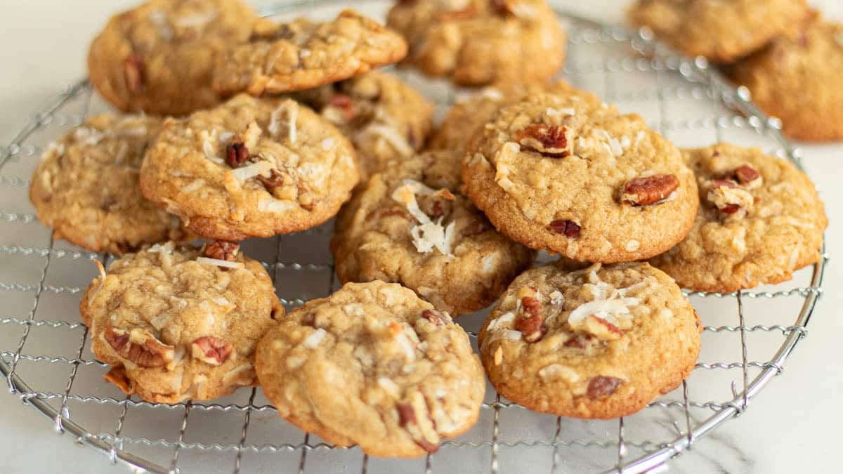 A batch of freshly baked cookies with nuts and coconut flakes cooling on a round wire rack.