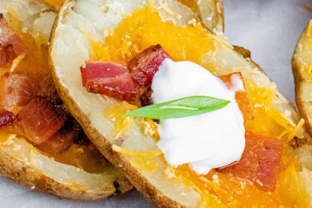 Potato skins topped with melted cheddar, bacon bits, a dollop of sour cream, and chives, making for an ideal potato side dish.