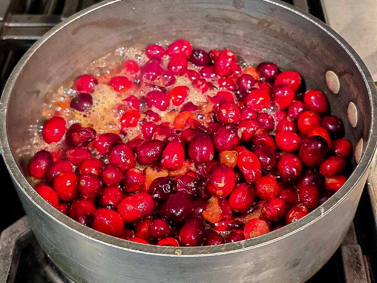 Cranberries simmering in a saucepan on a stovetop.