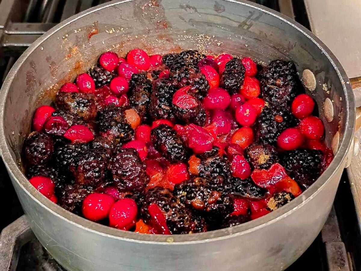A saucepan filled with a simmering mixture of blackberries and cranberries.