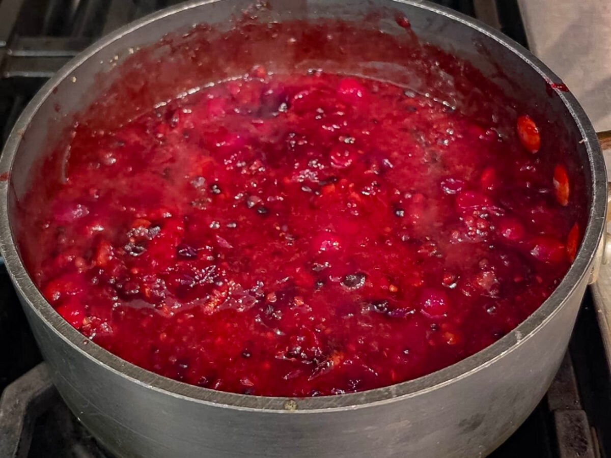 Cranberry sauce simmering in a metal pot on a stovetop.