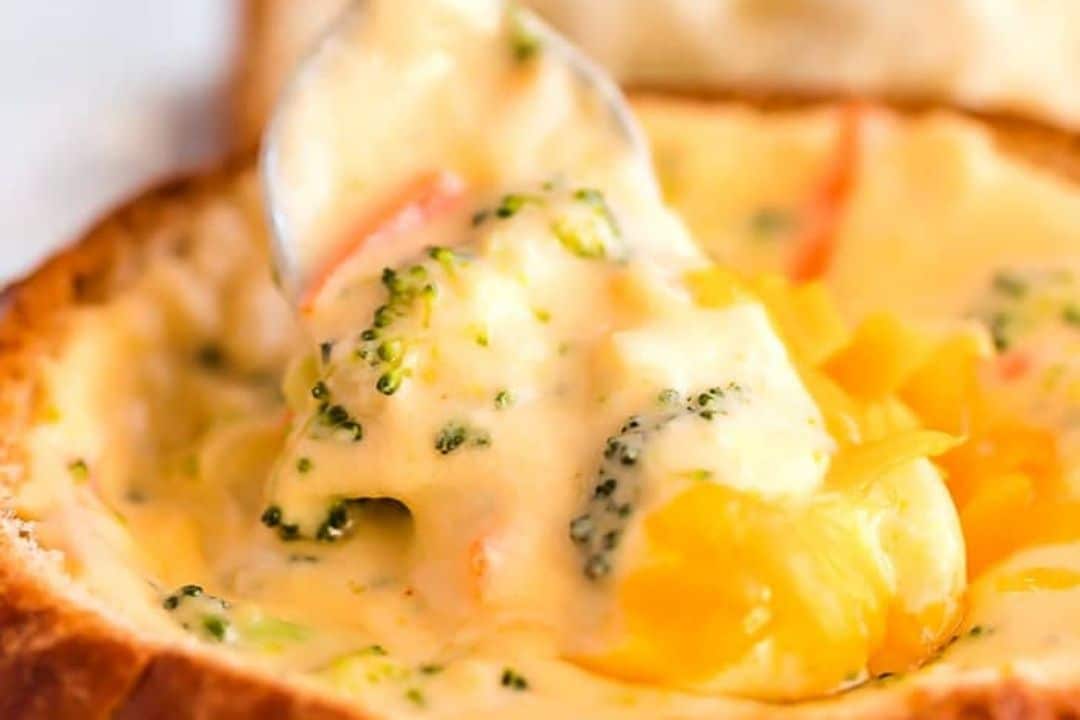 A spoonful of comforting broccoli cheddar soup served in a bread bowl.