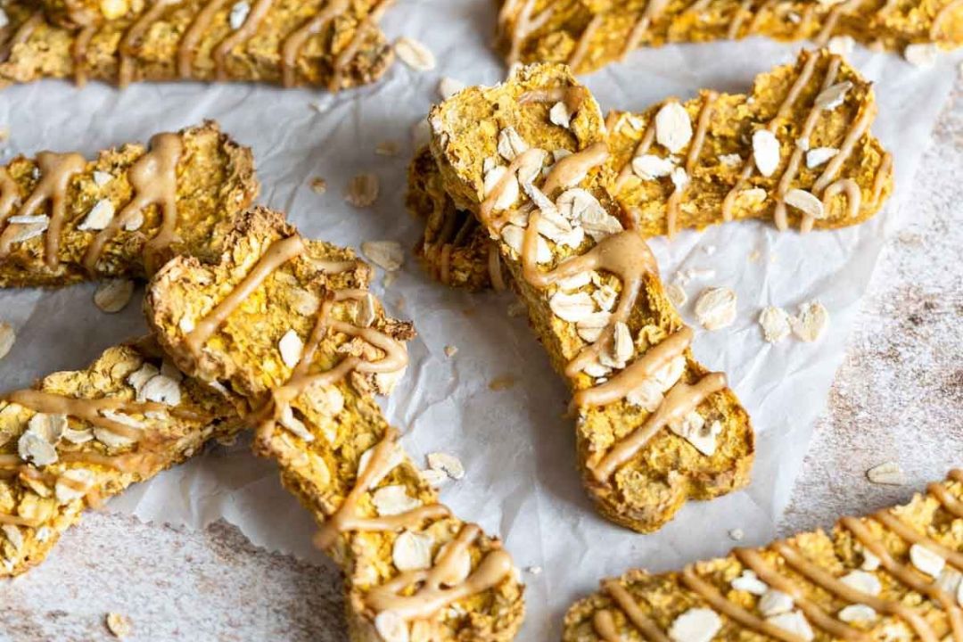 Bone-shaped dog treats drizzled with nut butter and topped with rolled oats.