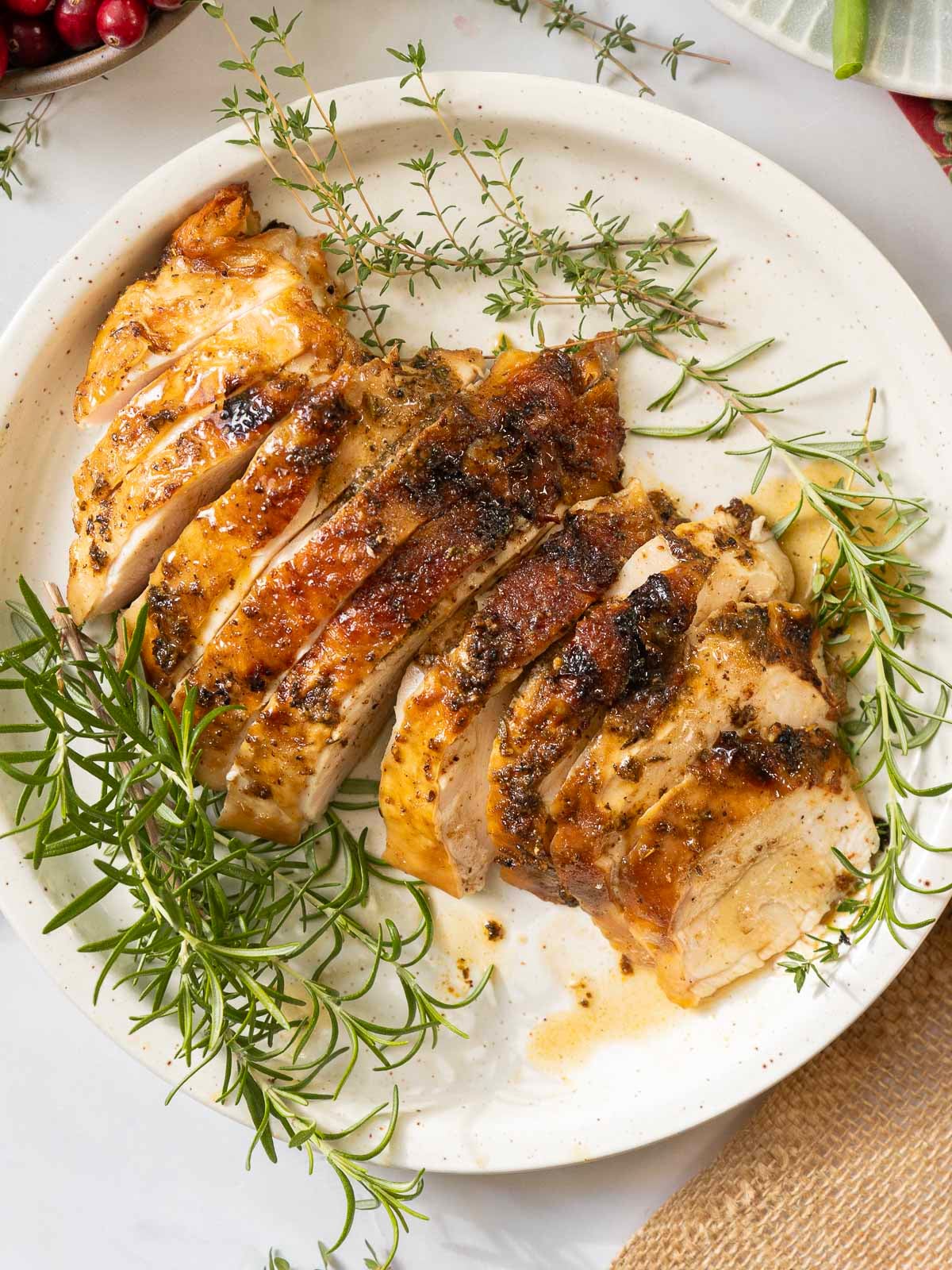 Sliced herb-roasted slow cooker turkey breast garnished with fresh rosemary and thyme on a white plate.