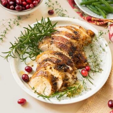Sliced slow cooker turkey breast garnished with fresh rosemary sprigs and cranberries on a white plate.