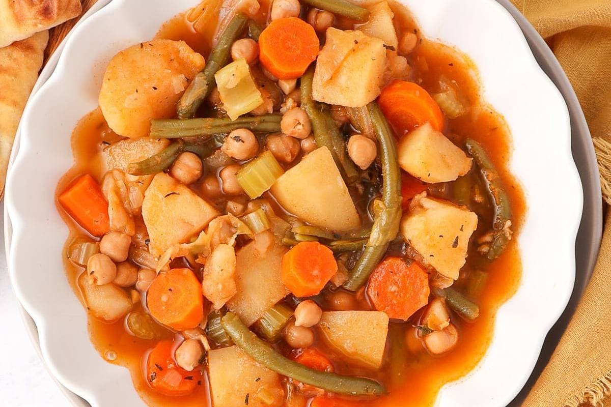 A comforting bowl of vegetable soup containing chickpeas, carrots, potatoes, and green beans.